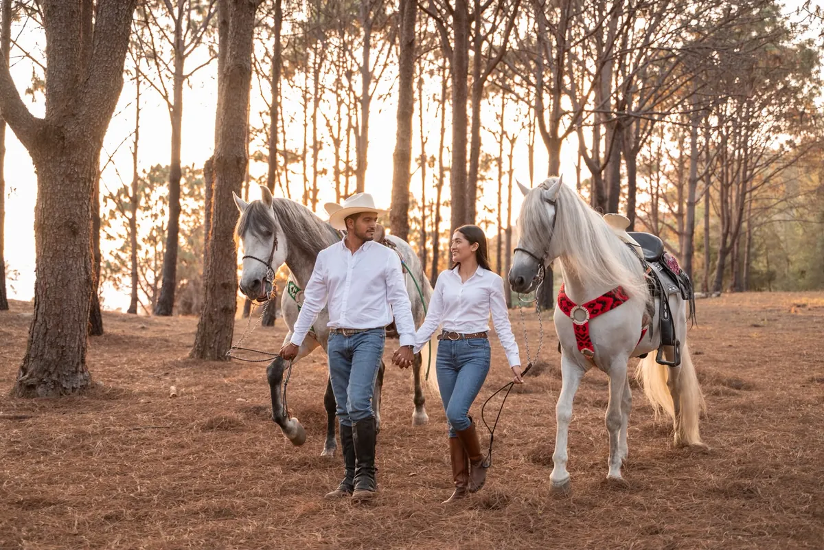Estephany y Jorge caminando entre los pinos con dos caballos blancos
